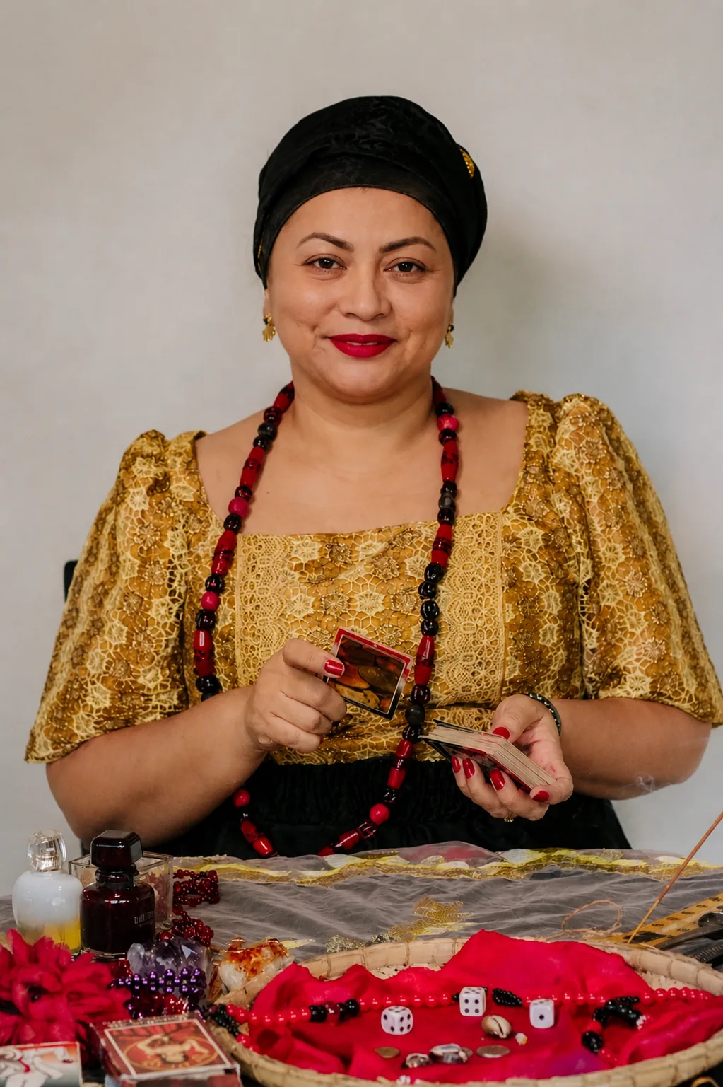 Mãe Lisandra de Iansã em consulta com cartas, búzios e mesa espiritual — renda dourada, turbante preto e guias vermelho e preto