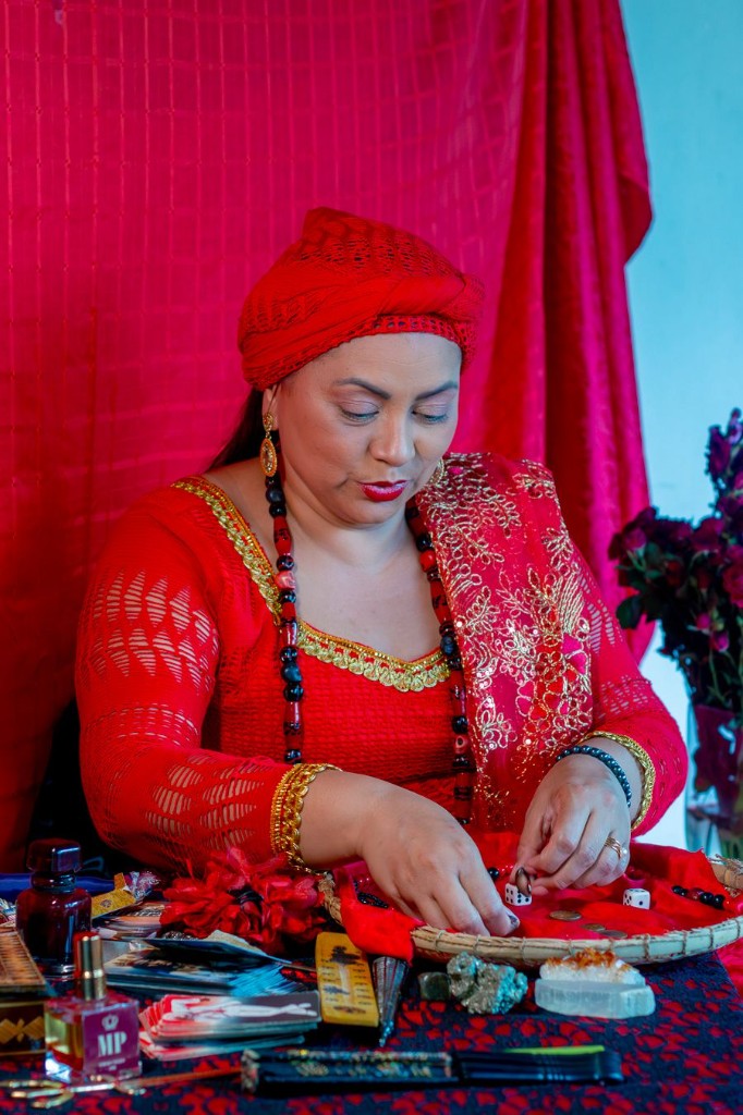 Leitura de cartas e ritual à mesa com baralho, perfumes e pedras — ambiente vermelho e dourado