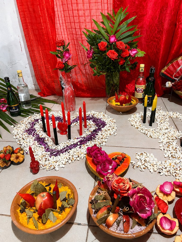 Oferendas no chão: coração de pipoca, velas, flores, frutas e itens de axé em trabalho voltado ao amor e à união